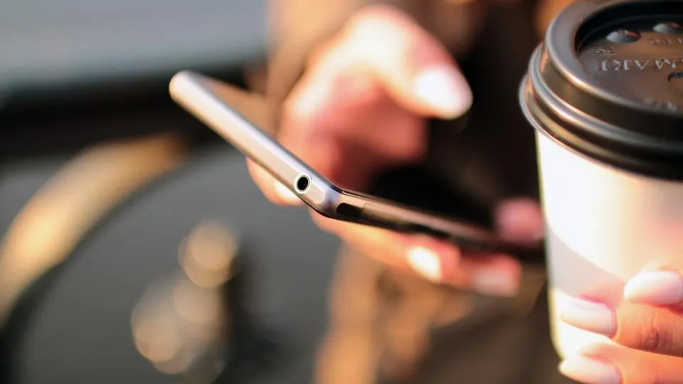 Ruka s mobilom a káva v pohári, zákazník sa objednáva online z telefónu