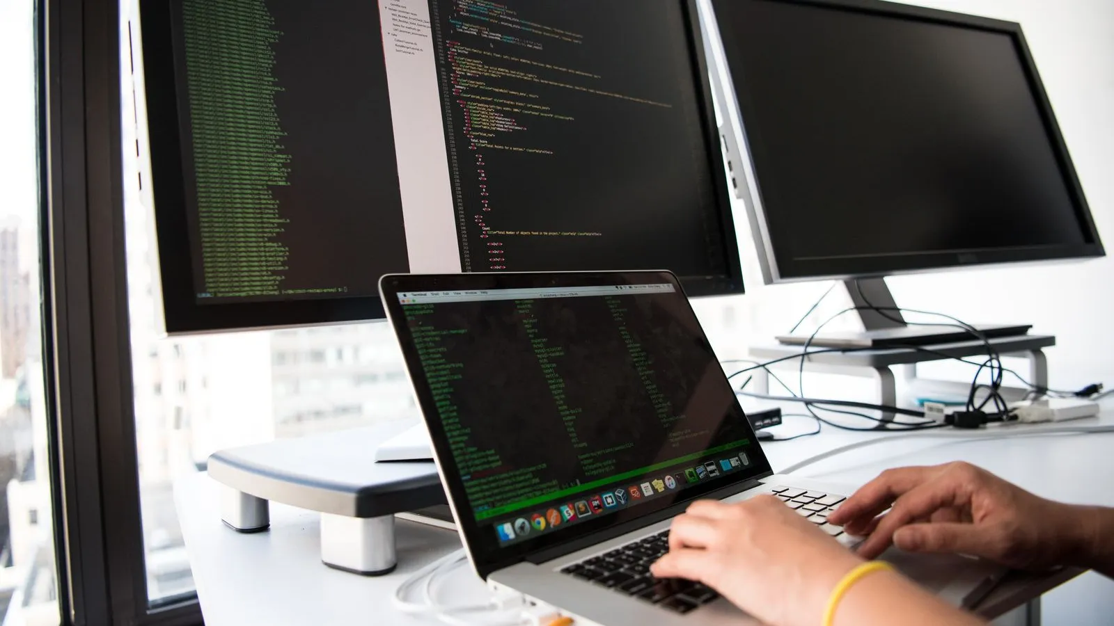 A developer at a laptop and two monitors with code – building a custom web application