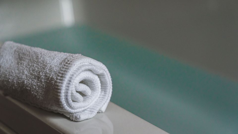 Zrolovaný biely uterák pri vani, wellness atmosféra salónu, web pre kaderníctvo