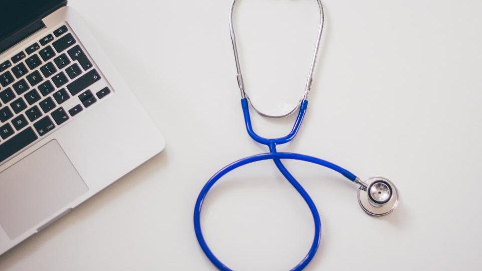 A stethoscope next to a laptop on a white desk, a website for a doctor and medical practice